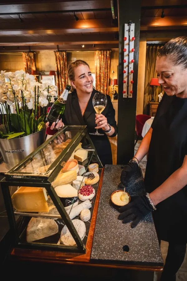 Onze fromagers Livia van IJperen en Ilkay Tinmaz bij de kaaskar, met een glas Champagne