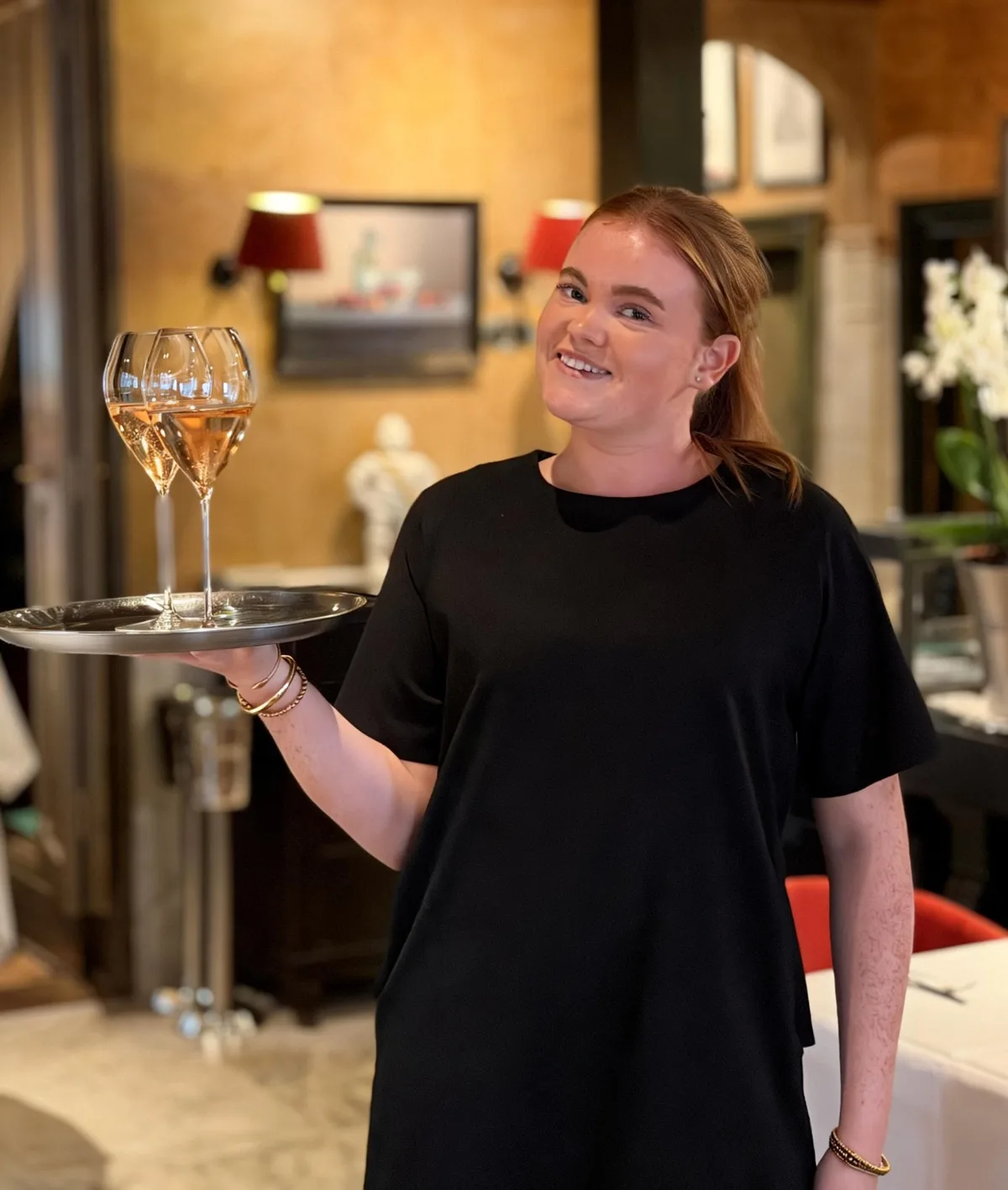 Een collega uit de bediening van Tante Koosje met twee glazen champagne op een dienblad, in de eetzaal