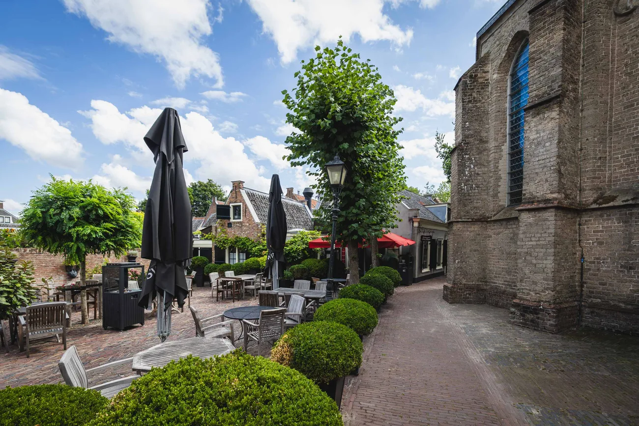 Het terras van Tante Koosje op het kerkplein, met parasols en buxus naast de oude dorpskerk
